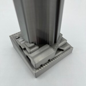 May include: A silver-colored 3D printed model of a skyscraper with a detailed base.