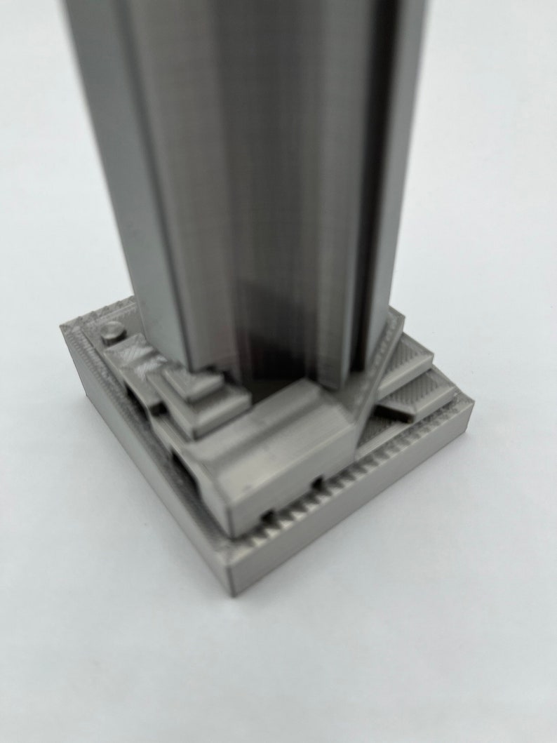 May include: A silver-colored 3D printed model of a skyscraper with a detailed base.