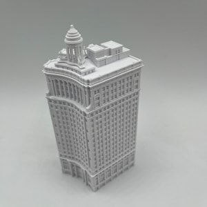 Op de afbeelding: Een wit 3D-geprint model van een hoog gebouw met een afgeronde hoek en een decoratieve bovenkant.