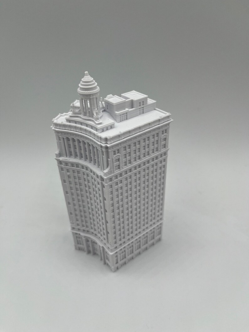 Op de afbeelding: Een wit 3D-geprint model van een hoog gebouw met een afgeronde hoek en een decoratieve bovenkant.
