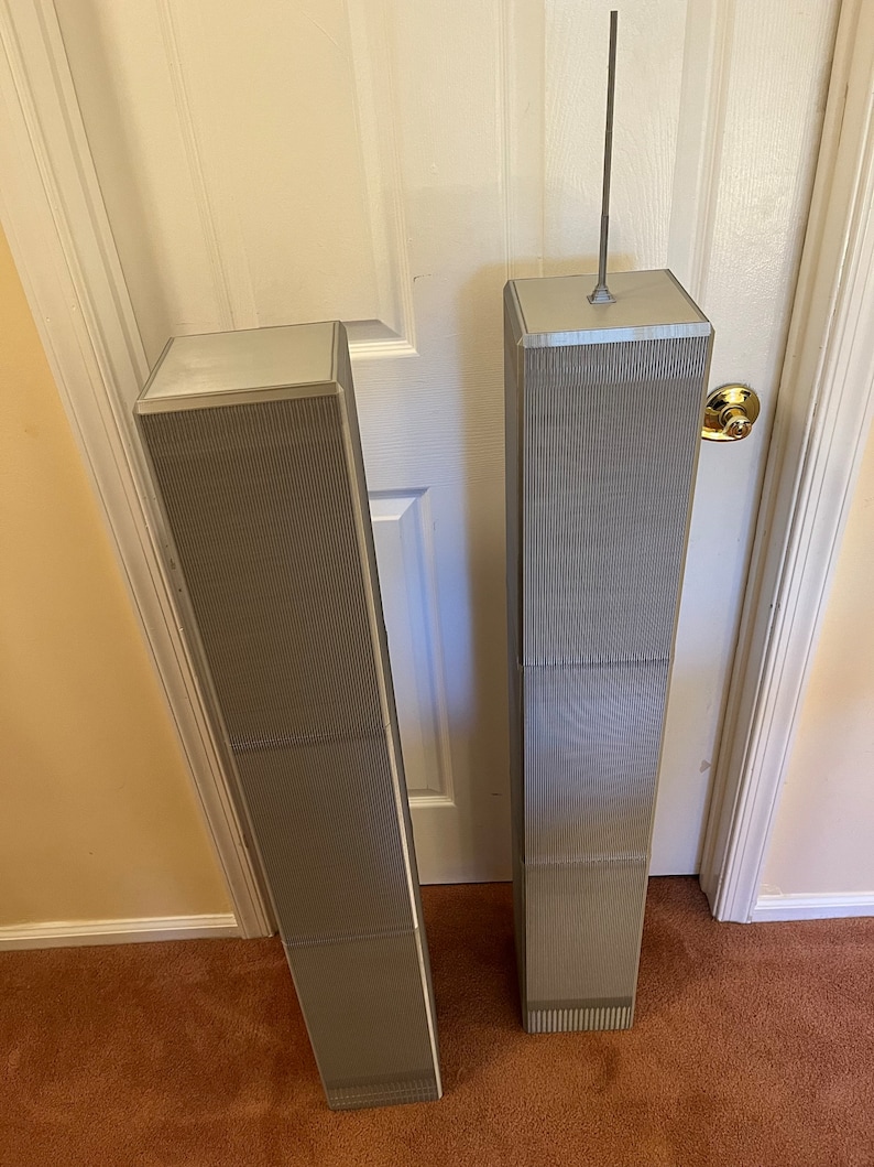 Pu&ograve; includere: Due modelli in miniatura delle Torri Gemelle, in argento e grigio. Gli edifici hanno una texture a coste sui lati e una parte superiore argentata. Un modello ha un'antenna argentata.