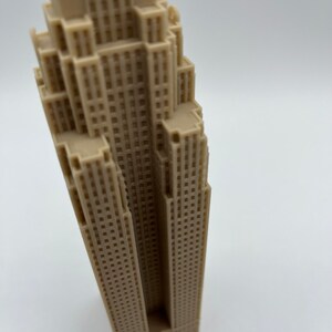 May include: A beige miniature model of a tall skyscraper with many windows.