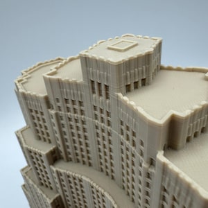 May include: A beige architectural model of a multi-storey building with a detailed facade. The model features multiple levels, windows, and a textured surface, showcasing a miniature cityscape design.