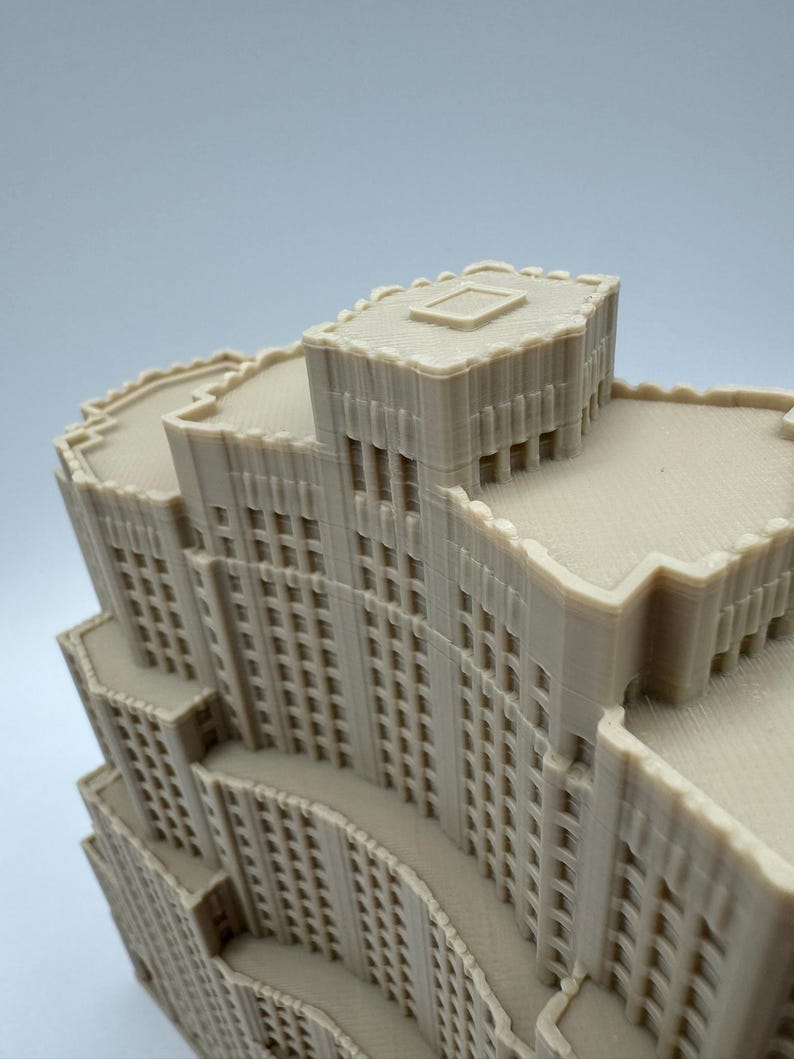 May include: A beige architectural model of a multi-storey building with a detailed facade. The model features multiple levels, windows, and a textured surface, showcasing a miniature cityscape design.
