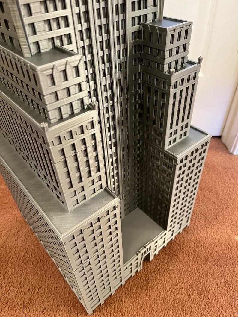 May include: A detailed model of a tall, gray skyscraper with many windows and a flat roof. The model is made of plastic and has a realistic appearance.