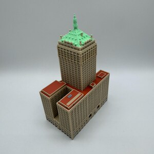 May include: A detailed miniature model of a skyscraper. The building features a tan facade, a green roof, and red accents. The model is a detailed replica of a famous building, perfect for collectors or architectural enthusiasts.