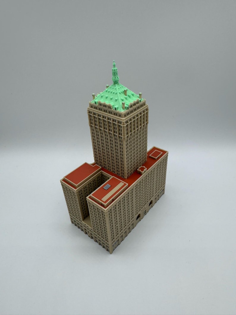 May include: A detailed miniature model of a skyscraper. The building features a tan facade, a green roof, and red accents. The model is a detailed replica of a famous building, perfect for collectors or architectural enthusiasts.