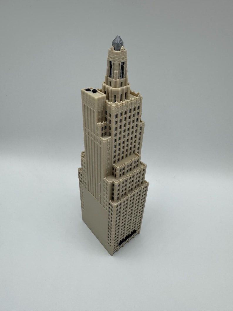 May include: A beige miniature skyscraper model with a detailed design. The building has multiple stories with rows of windows and a decorative top. The model is made of a light-colored material and stands upright against a white background.