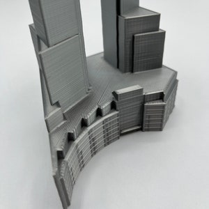 Op de afbeelding: Een 3D-geprint model van een moderne wolkenkrabber met een gebogen basis en een hoge, rechthoekige toren.