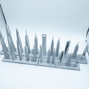 May include: A collection of miniature silver-colored skyscraper models, including the Burj Khalifa and the Empire State Building, arranged on a rectangular base. The models vary in height and design, showcasing architectural diversity.