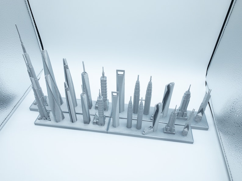 May include: A collection of miniature silver-colored skyscraper models, including the Burj Khalifa and the Empire State Building, arranged on a rectangular base. The models vary in height and design, showcasing architectural diversity.