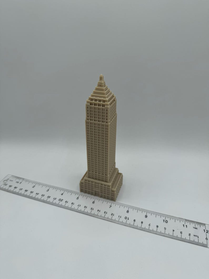 Puede incluir: Un modelo en miniatura beige de un rascacielos con un techo puntiagudo y muchas ventanas. El modelo mide aproximadamente 18 cm de alto y est&aacute; sentado sobre una superficie blanca junto a una regla.