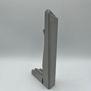 May include: A 3D printed model of a skyscraper, with a gray metallic finish. The model is detailed with a textured surface and a sharp, angular design.