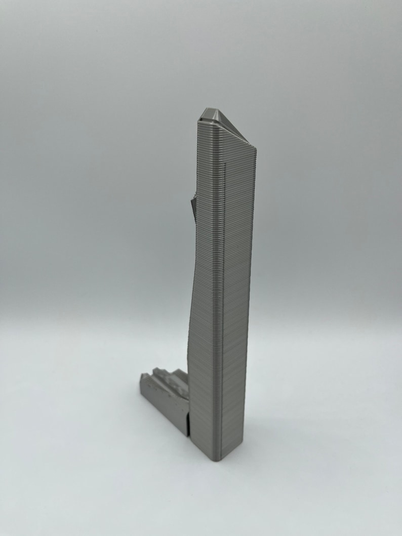 May include: A 3D printed model of a skyscraper, with a gray metallic finish. The model is detailed with a textured surface and a sharp, angular design.