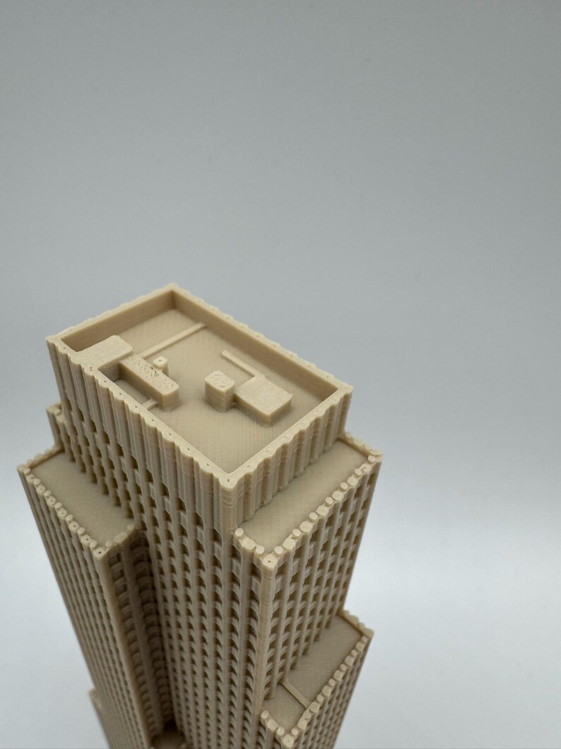 May include: A beige, 3D-printed model of a skyscraper. The building has multiple tiers and a flat roof with architectural details. The windows are small and evenly spaced. The model is set against a plain white background.