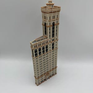 May include: A detailed model of a tall, beige building with a distinctive architectural design. The building has numerous windows, decorative trim, and a tower at the top. The model is set against a plain background.