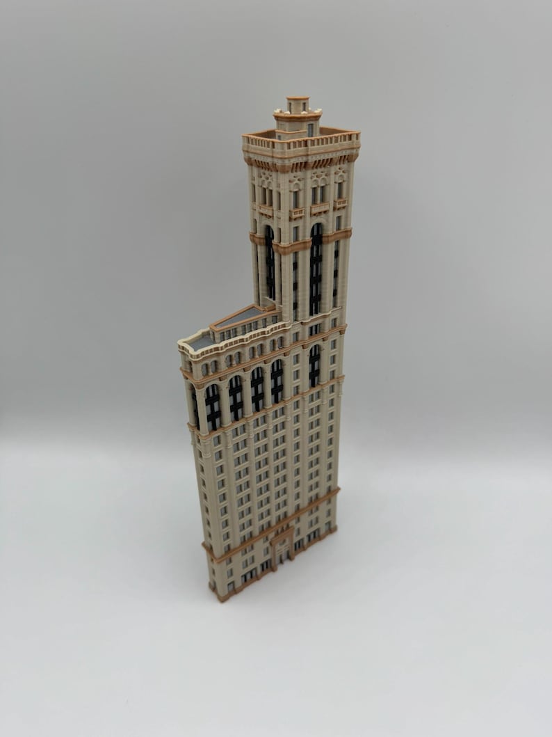 May include: A detailed model of a tall, beige building with a distinctive architectural design. The building has numerous windows, decorative trim, and a tower at the top. The model is set against a plain background.