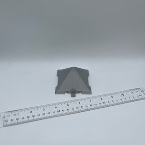 Puede incluir: Un objeto gris en forma de pir&aacute;mide con una regla al lado. La pir&aacute;mide tiene una parte superior plana y una base rectangular. La regla es transparente y est&aacute; marcada con cent&iacute;metros, mostrando el tama&ntilde;o del objeto.