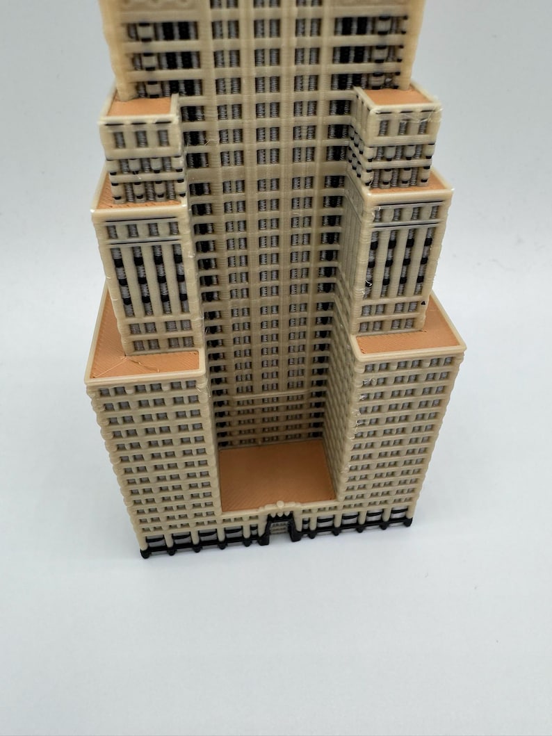 May include: A beige and brown 3D-printed model of a skyscraper. The building features numerous windows and architectural details, with a rectangular base and multiple tiers. The model is set against a white background.