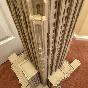 Puede incluir: Un modelo impreso en 3D detallado de un edificio alto con un techo puntiagudo y detalles intrincados. El modelo est&aacute; hecho de pl&aacute;stico marr&oacute;n claro y tiene una superficie texturizada.