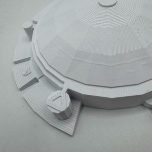 May include: A 3D-printed model of a domed structure, likely a building or architectural element. The model is white and features a detailed, layered design with geometric patterns. The structure includes a circular base and several cylindrical elements.