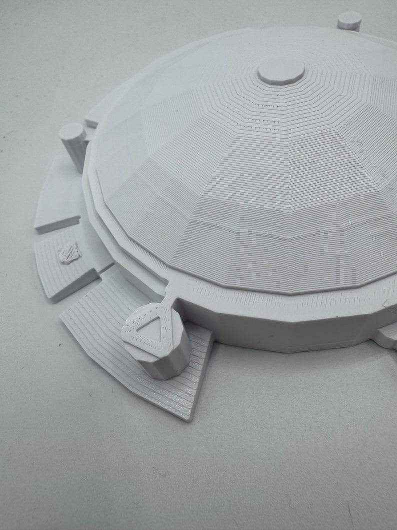 May include: A 3D-printed model of a domed structure, likely a building or architectural element. The model is white and features a detailed, layered design with geometric patterns. The structure includes a circular base and several cylindrical elements.