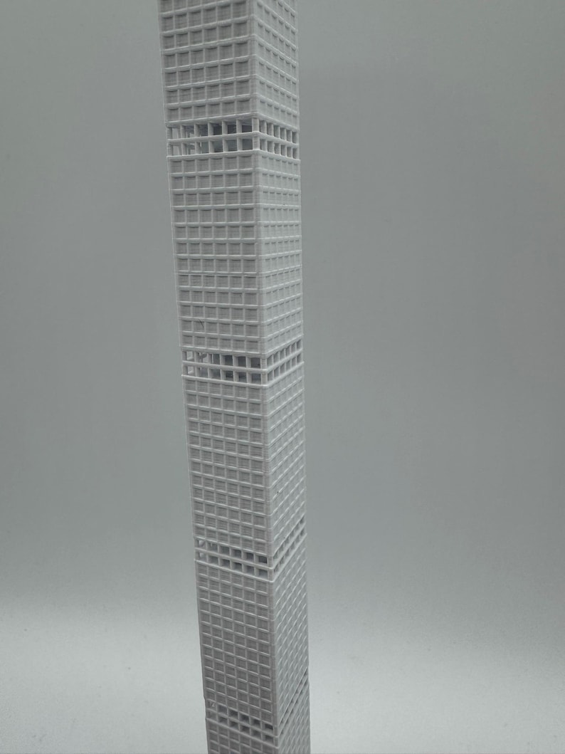 May include: A grey model of a skyscraper with a grid-like facade. The building is rectangular and tapers slightly towards the top. The model is a detailed representation of a modern architectural design.