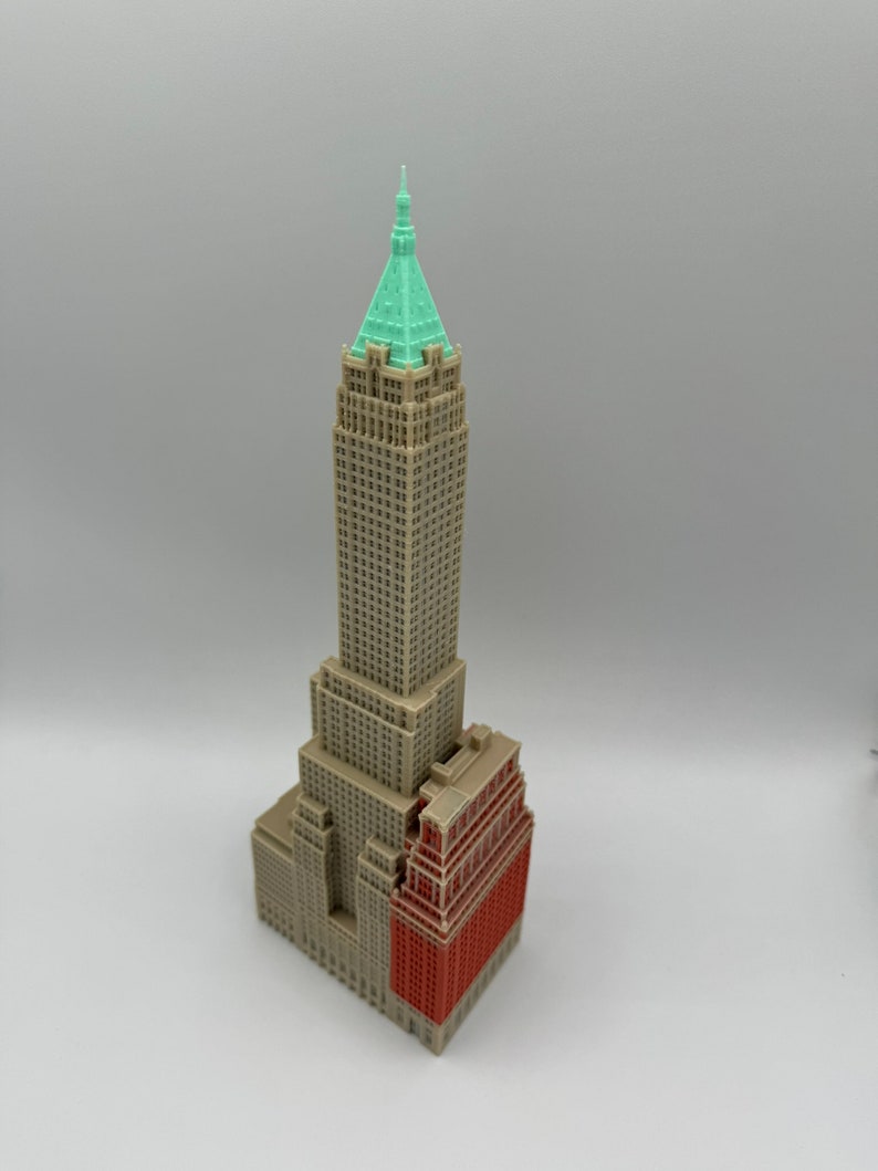 May include: A miniature model of a skyscraper with a green roof and a red brick base. The building is made of beige plastic and has many windows.