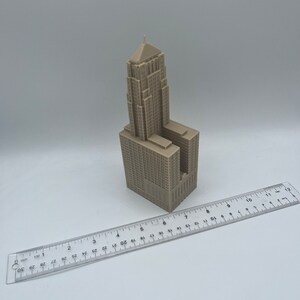 May include: A beige 3D printed model of a tall building with a pointed roof. The model is about 6 inches tall and is sitting on a white surface.