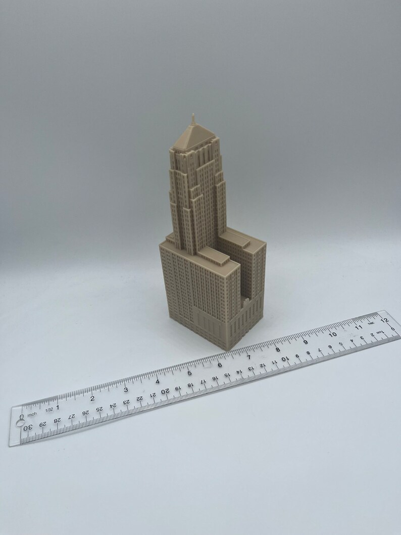 May include: A beige 3D printed model of a tall building with a pointed roof. The model is about 6 inches tall and is sitting on a white surface.