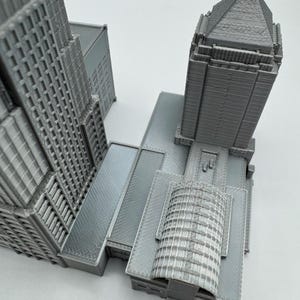 May include: A gray architectural model of a skyscraper complex. The model features detailed facades, multiple towers, and various roof designs. The overall structure is a monochromatic gray, with visible textures and architectural details.