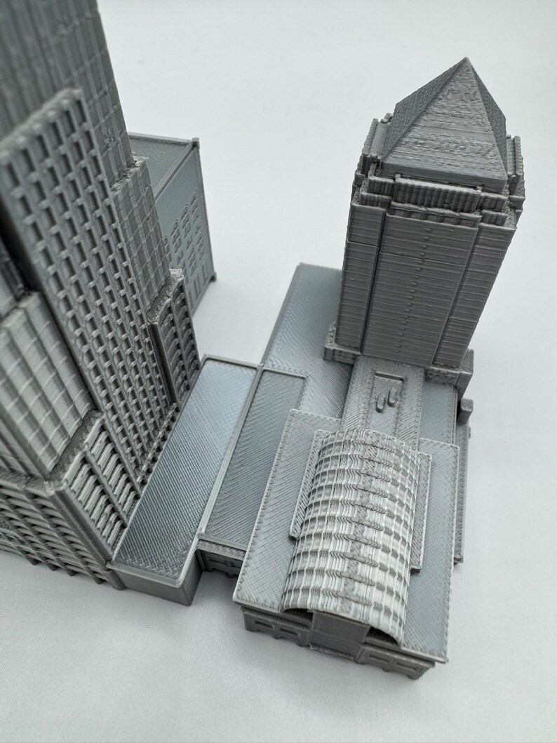 May include: A gray architectural model of a skyscraper complex. The model features detailed facades, multiple towers, and various roof designs. The overall structure is a monochromatic gray, with visible textures and architectural details.