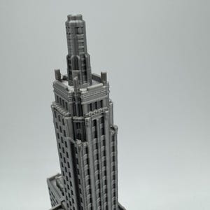 May include: A 3D printed model of a tall, grey building with a pointed roof and many windows.