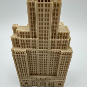 May include: A detailed 3D printed model of a tall, beige building with many windows. The building has a flat roof and a decorative cornice.