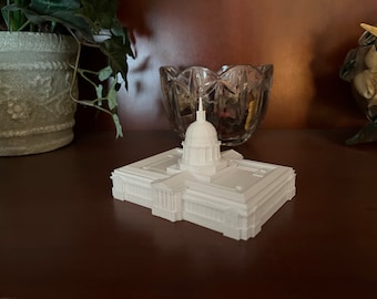 Puede incluir: Un modelo 3D impreso en blanco de un edificio con una cúpula en la parte superior. El modelo está sentado sobre una superficie marrón.