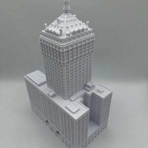 Puede incluir: Modelo arquitect&oacute;nico blanco detallado de un rascacielos. El modelo presenta una torre central alta con una parte superior decorativa y una base m&aacute;s ancha con m&uacute;ltiples niveles. El edificio tiene muchas ventanas y detalles arquitect&oacute;nicos.