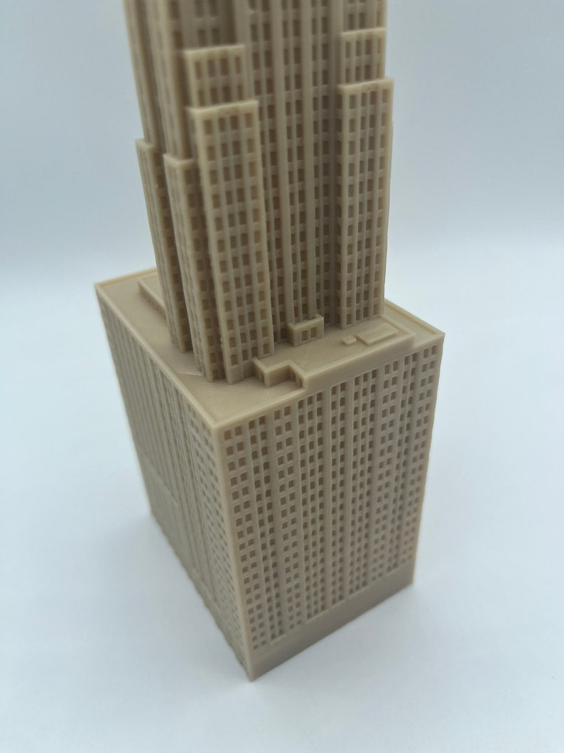 May include: A detailed model of a skyscraper, made of a light brown plastic material. The model is a miniature replica of a tall building with many windows and a flat roof.