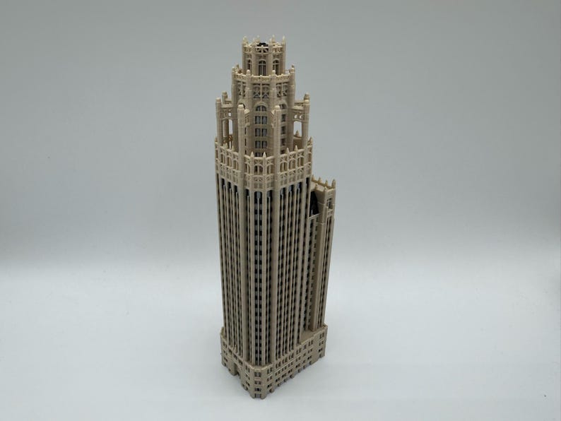 May include: A beige, three-dimensional architectural model of a skyscraper featuring a stepped, multi-tiered design with intricate vertical detailing, arched window patterns, and a central tower structure that tapers toward the top.