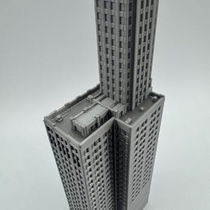 May include: A grey 3D printed model of a tall skyscraper building with a flat roof.