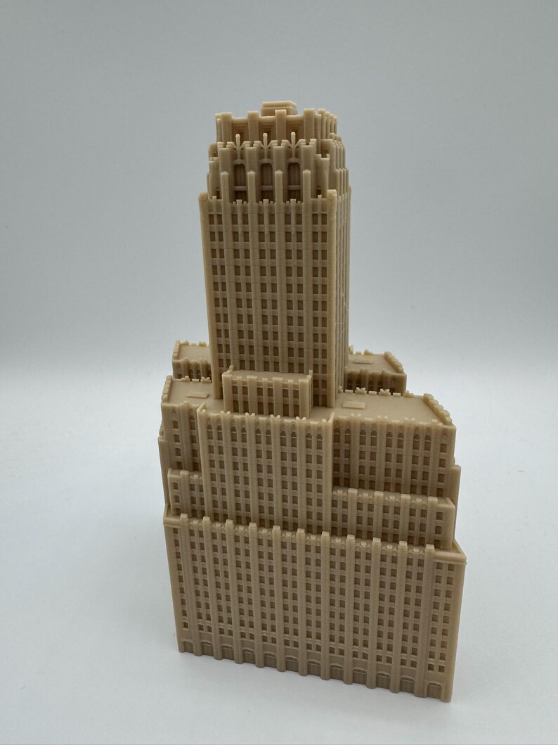 May include: A tan-colored miniature skyscraper model with a detailed facade. The building has multiple tiers and a tall central tower, featuring numerous windows and architectural details. The model is likely made of plastic or resin.