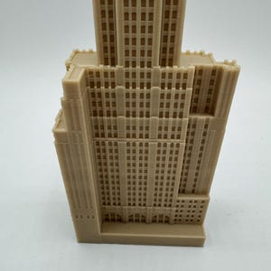 May include: A beige 3D printed model of a tall building with many windows. The model is detailed and has a base.