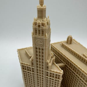 May include: A beige miniature of a tall building with a clock tower. The building has many windows and architectural details. The model is likely a replica of a famous landmark.