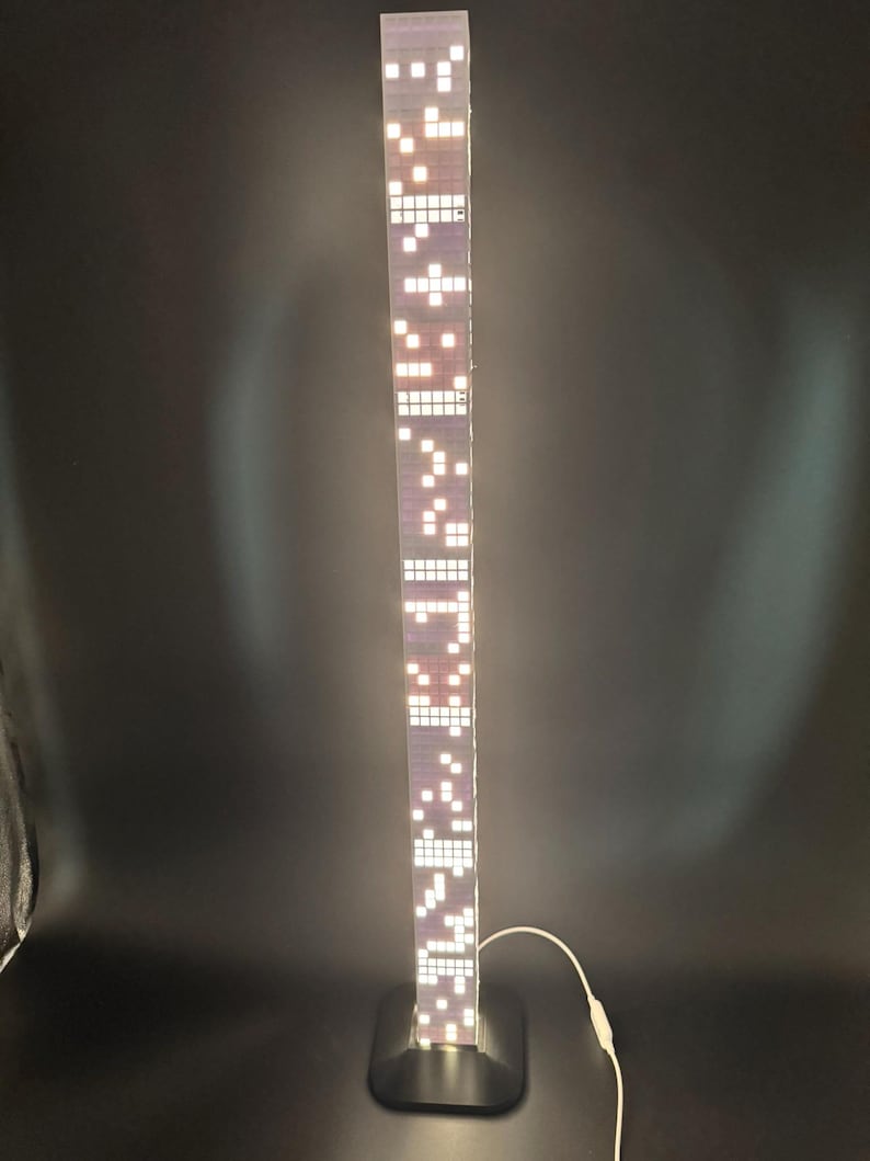 May include: A tall, rectangular LED lamp with a black base. The lamp's body is a series of illuminated white squares against a purple background, resembling a skyscraper. A white cord extends from the base.