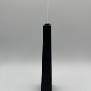 May include: A black architectural model of a skyscraper with a detailed facade. Two thin, white antennae extend from the top of the building. The model is set against a plain, light gray background.