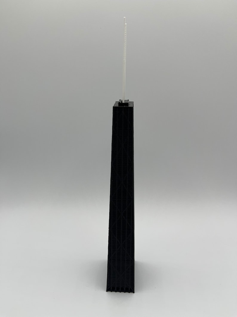 May include: A black architectural model of a skyscraper with a detailed facade. Two thin, white antennae extend from the top of the building. The model is set against a plain, light gray background.