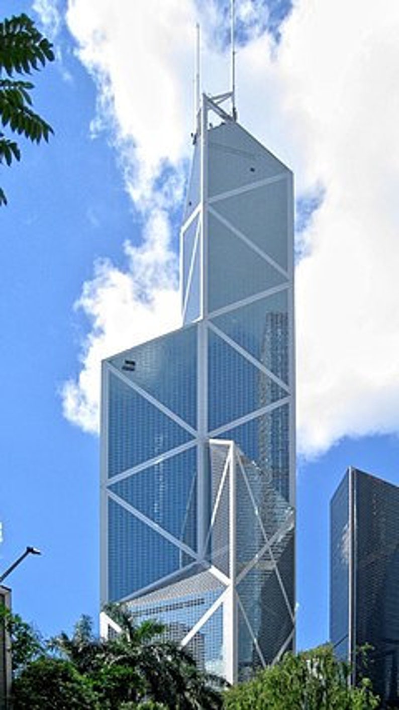 May include: A tall, modern skyscraper with a unique geometric design. The building features a white frame with triangular and rectangular glass panels. The sky is blue with fluffy white clouds, and green trees are visible at the base of the building.