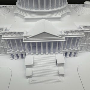 K&ouml;nnte beinhalten: Ein detailliertes, wei&szlig;es 3D-gedrucktes Modell eines Geb&auml;udes mit einer gro&szlig;en Kuppel, S&auml;ulen und mehreren Ebenen. Das Modell weist komplizierte architektonische Details auf, darunter Treppen und ein symmetrisches Design.