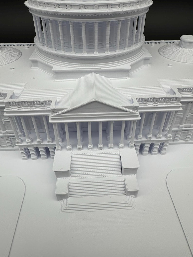 K&ouml;nnte beinhalten: Ein detailliertes, wei&szlig;es 3D-gedrucktes Modell eines Geb&auml;udes mit einer gro&szlig;en Kuppel, S&auml;ulen und mehreren Ebenen. Das Modell weist komplizierte architektonische Details auf, darunter Treppen und ein symmetrisches Design.