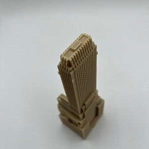 May include: A beige miniature model of a skyscraper with a detailed facade and a flat roof.