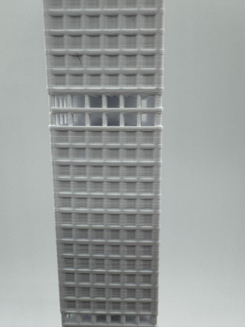 May include: A 3D-printed model of a skyscraper. The building is a light grey colour and features a grid-like pattern of windows and structural elements. The model is a detailed representation of a modern architectural design.